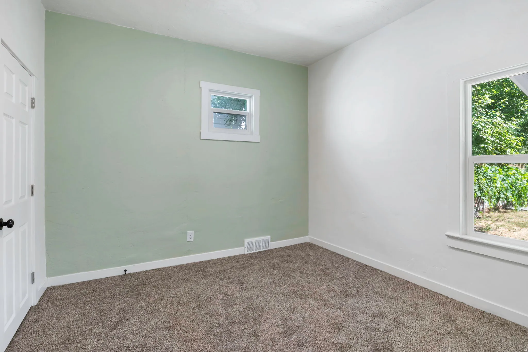 Carpeted room featuring a white door with a black knob, a single window with white trim, a second window with white trim, and a light green accent wall