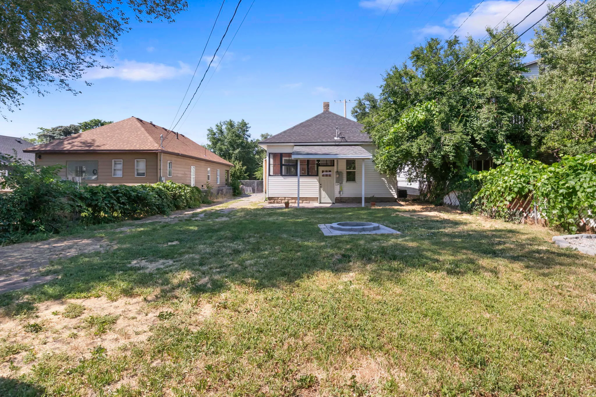 Spacious backyard featuring a built-in fire pit, mature trees, and a covered porch entry