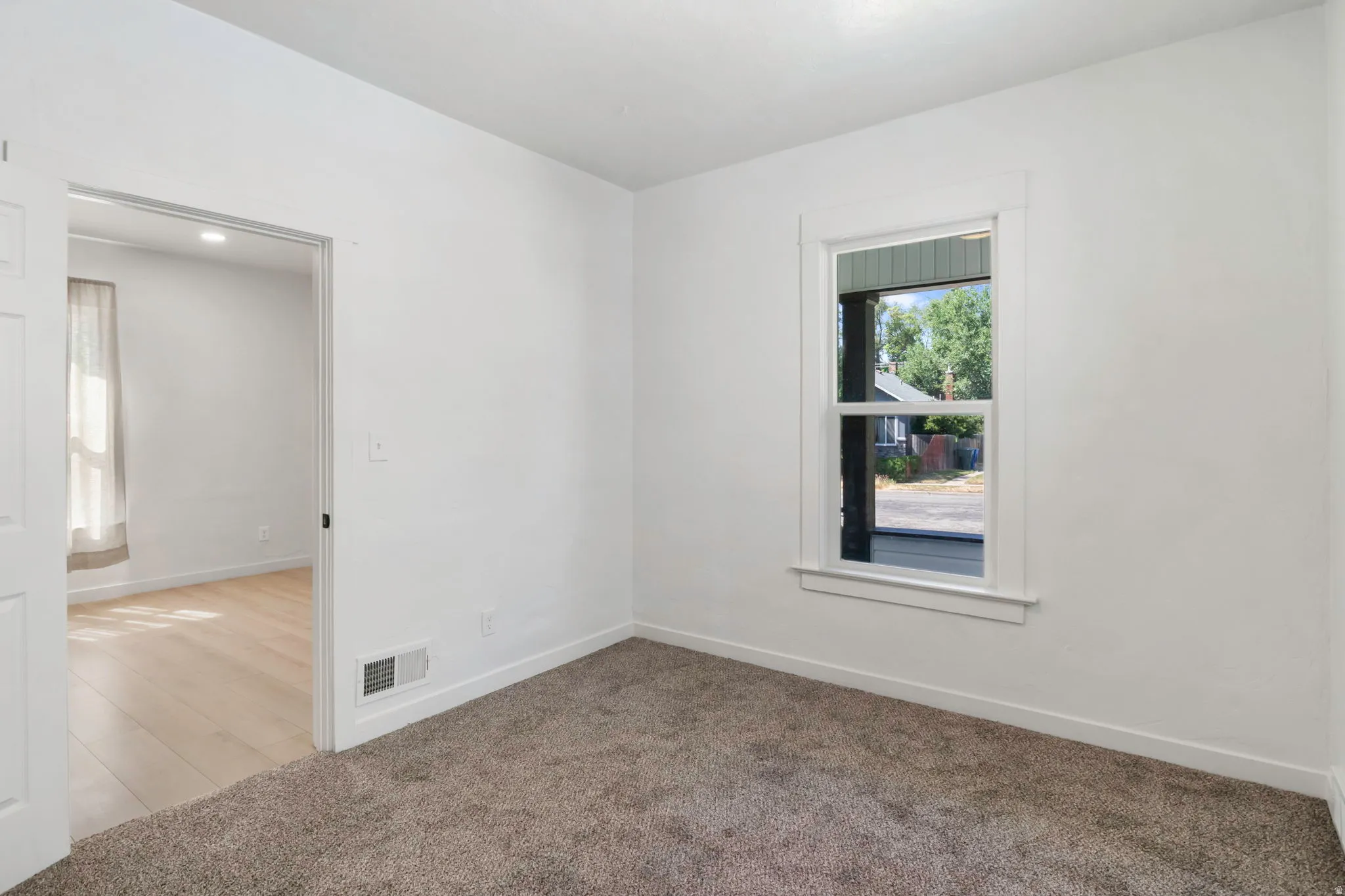 Room featuring neutral-toned carpeting, white walls, and a single window with white trim