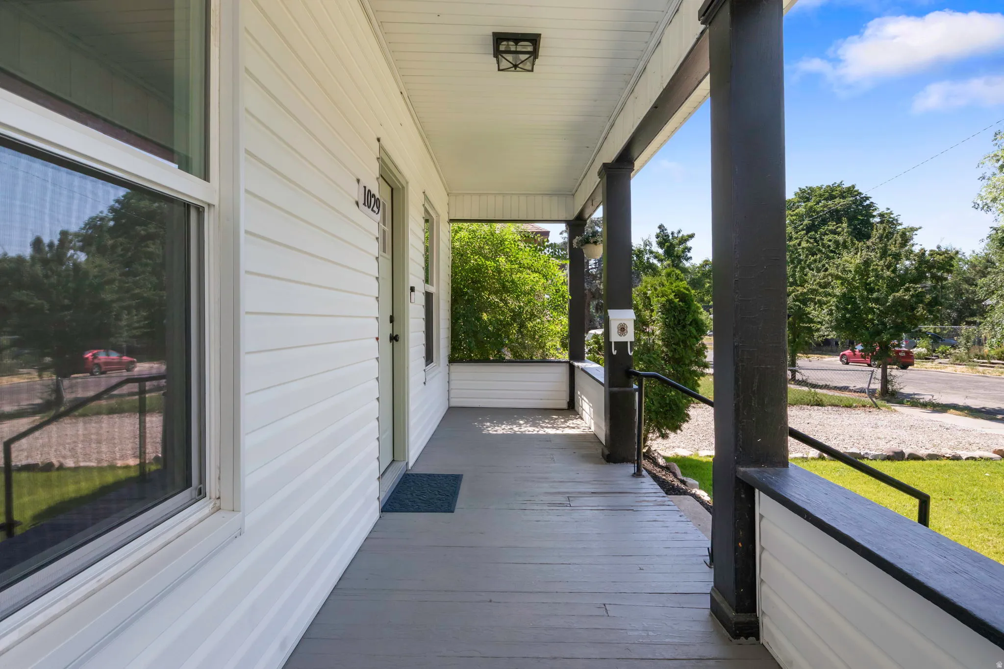 Covered front porch featuring white siding, dark support columns, black railings, and a contrasting gray floor