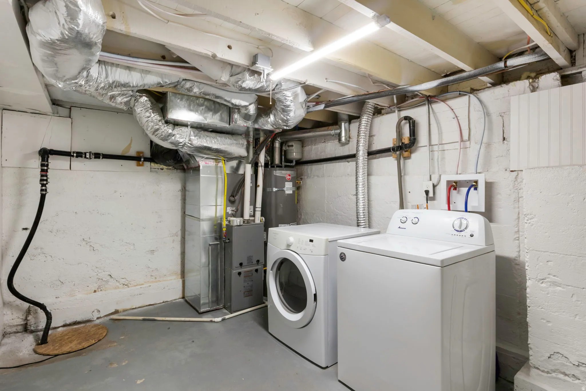 Utility area featuring exposed overhead ductwork, fluorescent lighting, and a sump pump