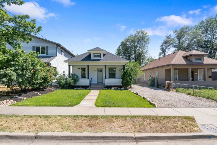Charming white siding exterior with a welcoming covered front porch, a well-maintained lawn, and a gravel driveway