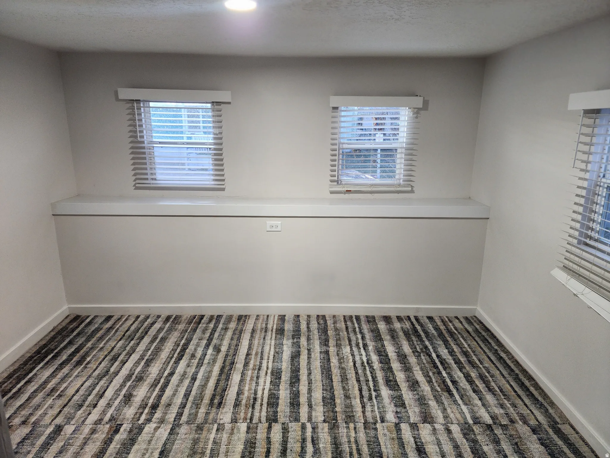 Room featuring a patterned area rug, two windows with blinds, a built-in shelf, and recessed lighting