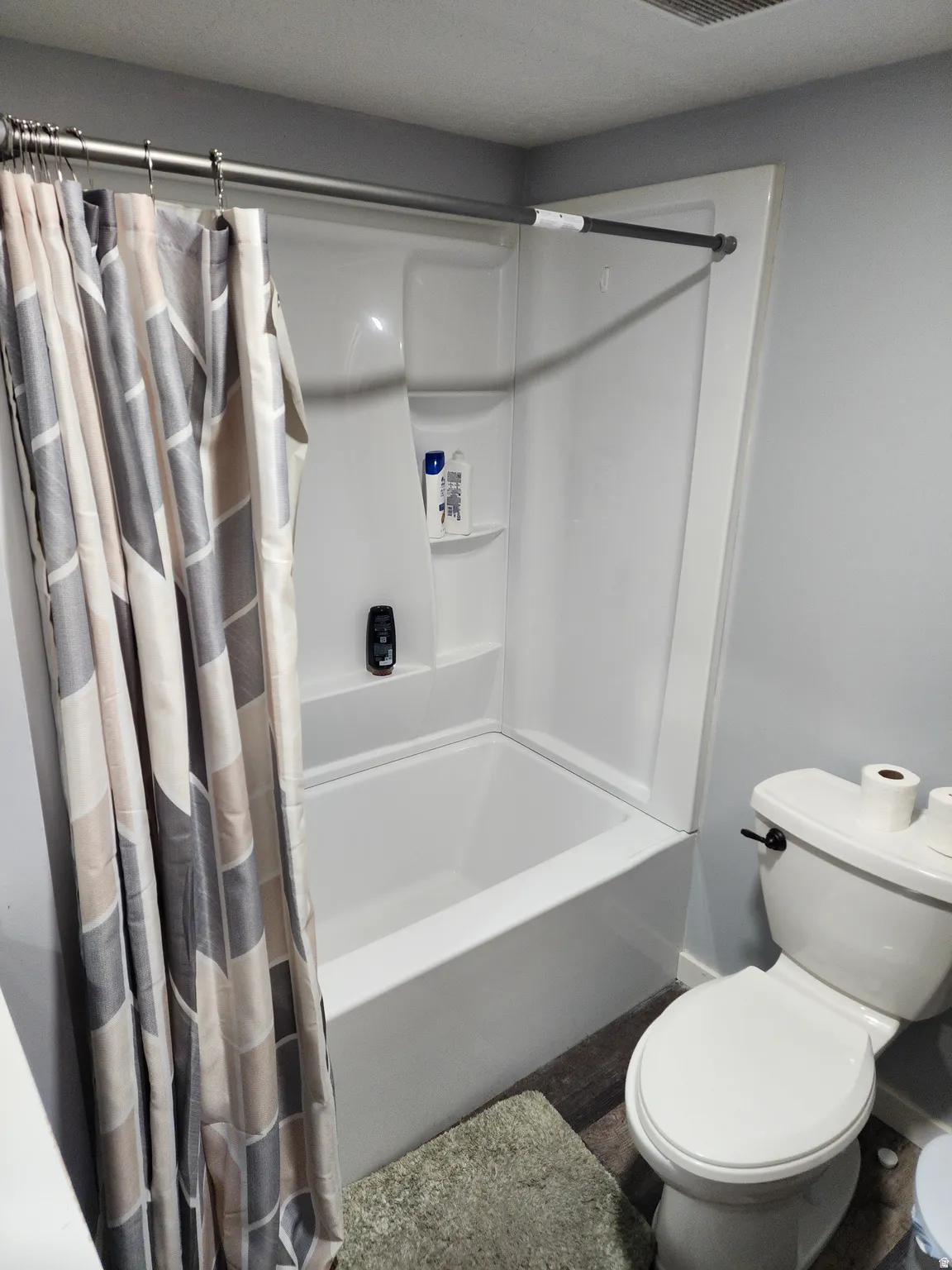 White fiberglass tub and shower combination with integrated shelving, accompanied by a white toilet