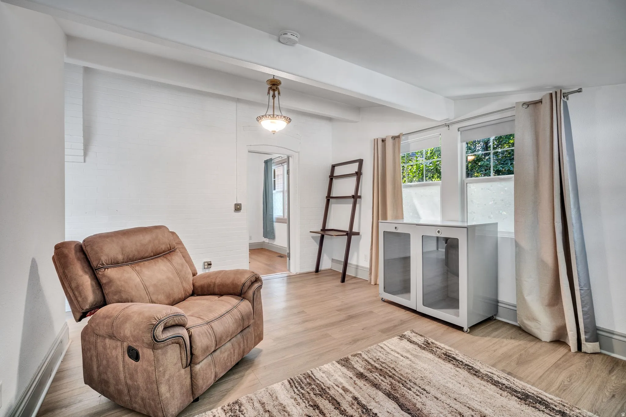 2-bedroom floorplan (614) bedroom #1featuring wood-finish flooring, white painted brick walls, exposed ceiling beams, and a decorative pendant light fixture
