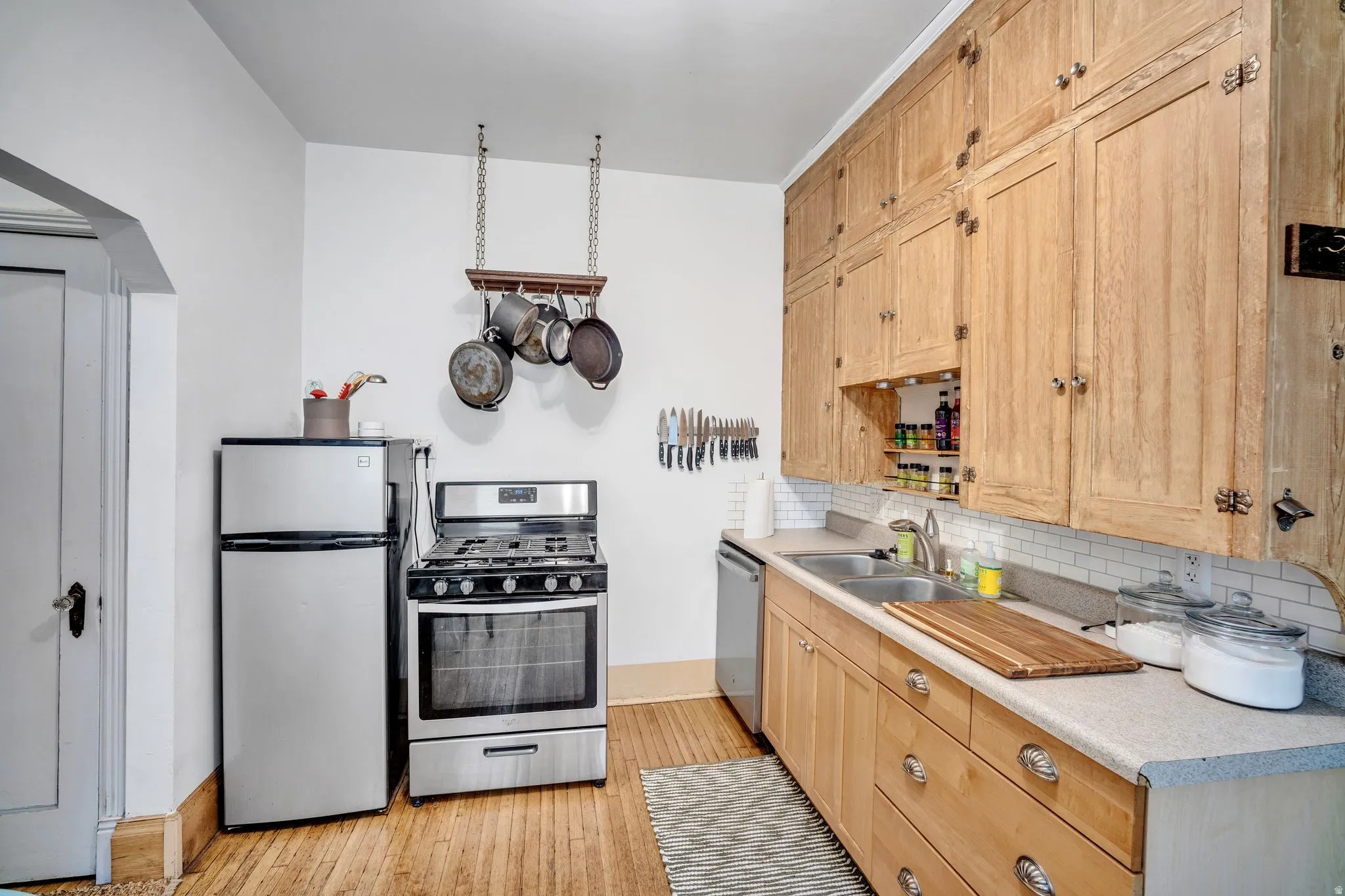 2-bedroom floorplan (614) kitchen featuring natural wood cabinetry, stainless steel appliances, a double basin sink, white subway tile backsplash, and wood-finish flooring