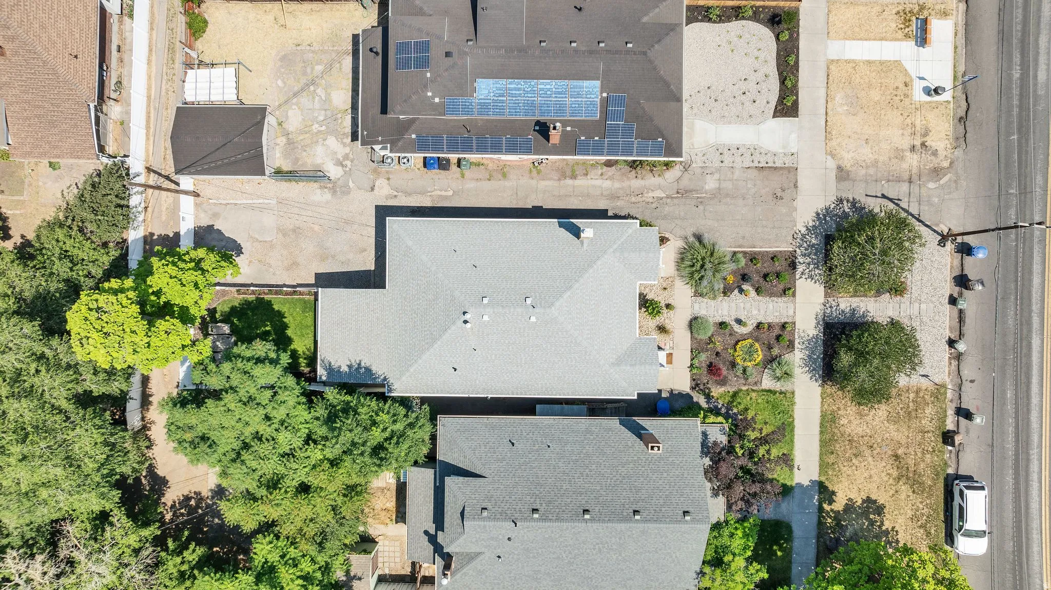 Property features a gray shingle roof, a structured front yard with diverse plantings, and mature trees providing natural screening