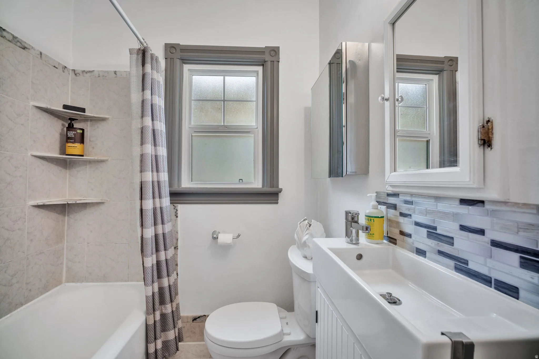 2-bedroom floorplan (614) bathroom featuring a white bathtub, tiled shower surround with corner shelves, and a window with decorative trim