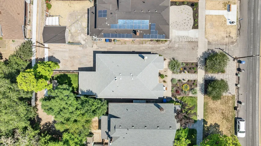 Property features a gray shingle roof, a structured front yard with diverse plantings, and mature trees providing natural screening