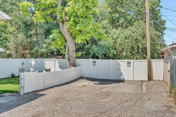 Gravel parking area featuring 2 off-street parking spaces, a white vinyl privacy fence and a mature tree