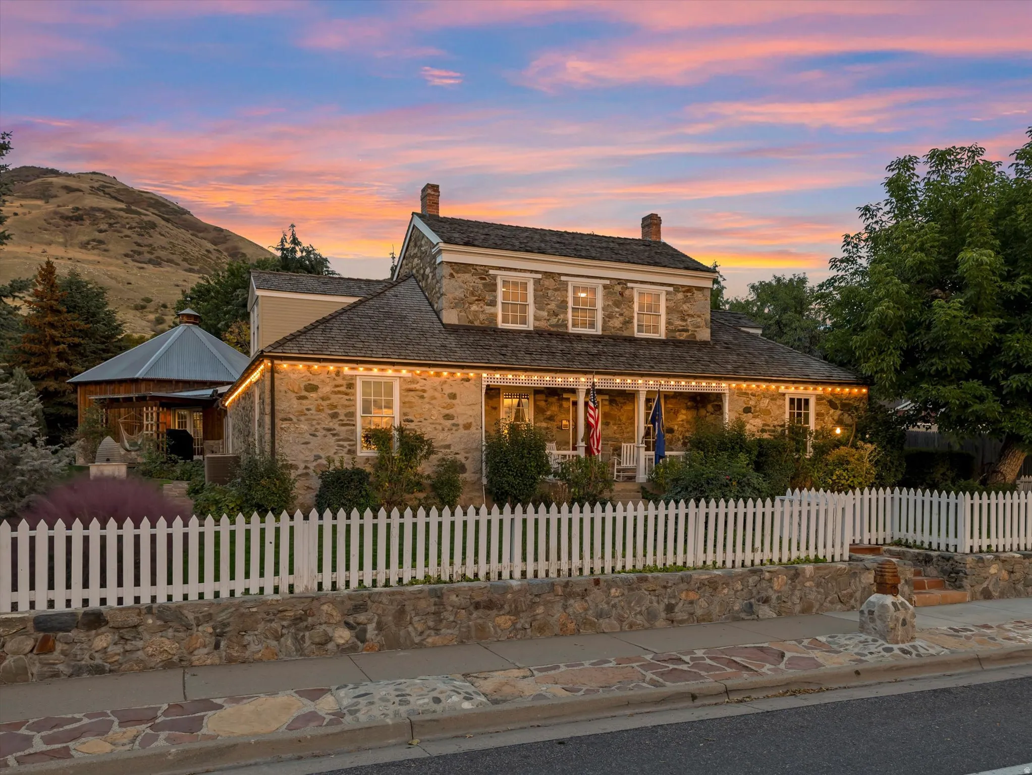 Stone exterior residence featuring a white picket fence, stone retaining wall, and a covered front porch