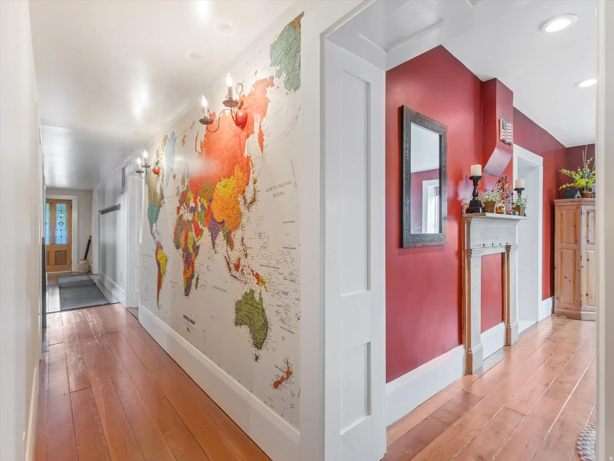 Hallway featuring wood-finish flooring, a decorative wall map, wall-mounted sconces, and a painted red wall