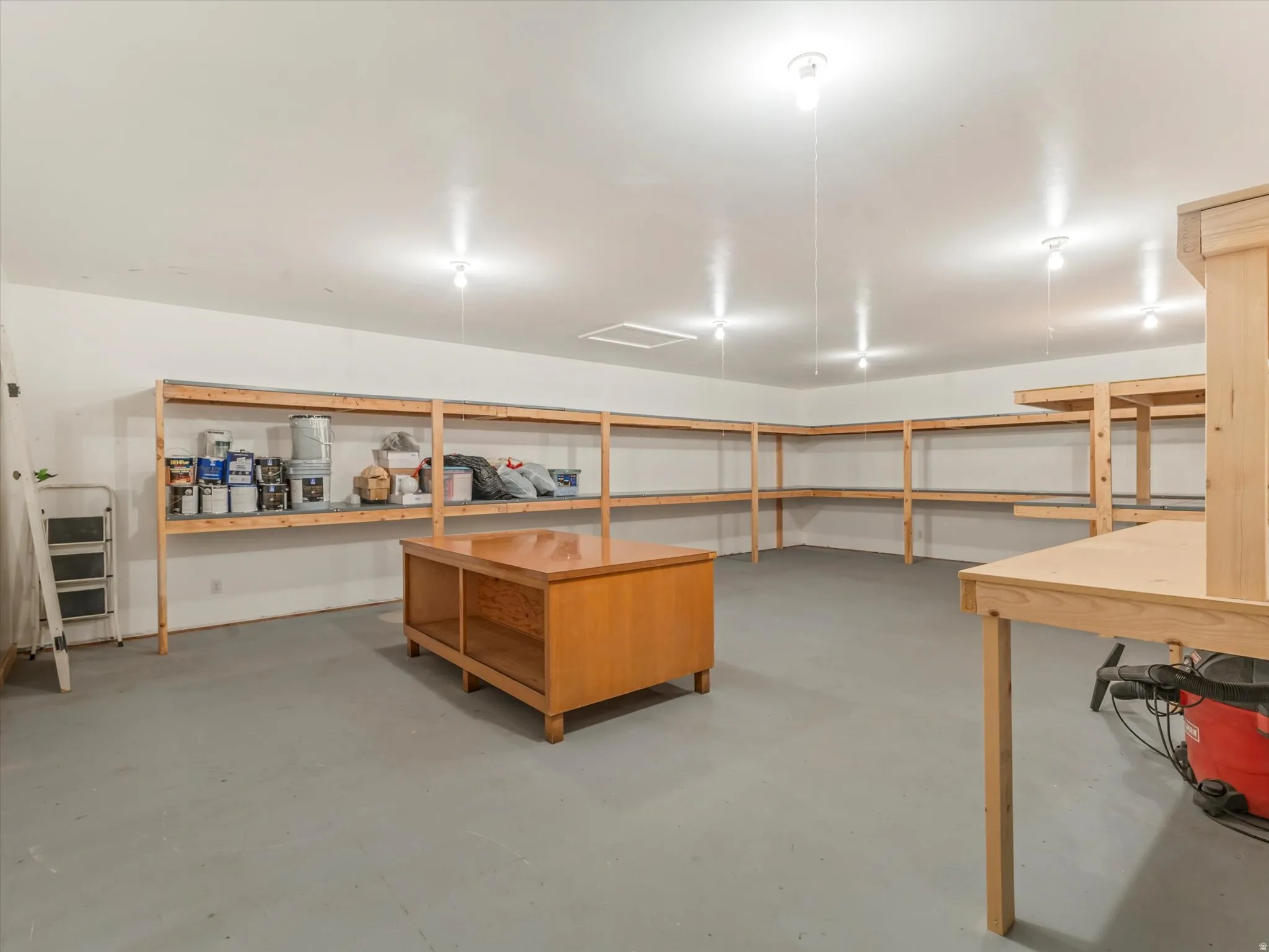 ADU Spacious utility room featuring extensive built-in wooden shelving, a painted concrete floor, and multiple ceiling-mounted light fixtures