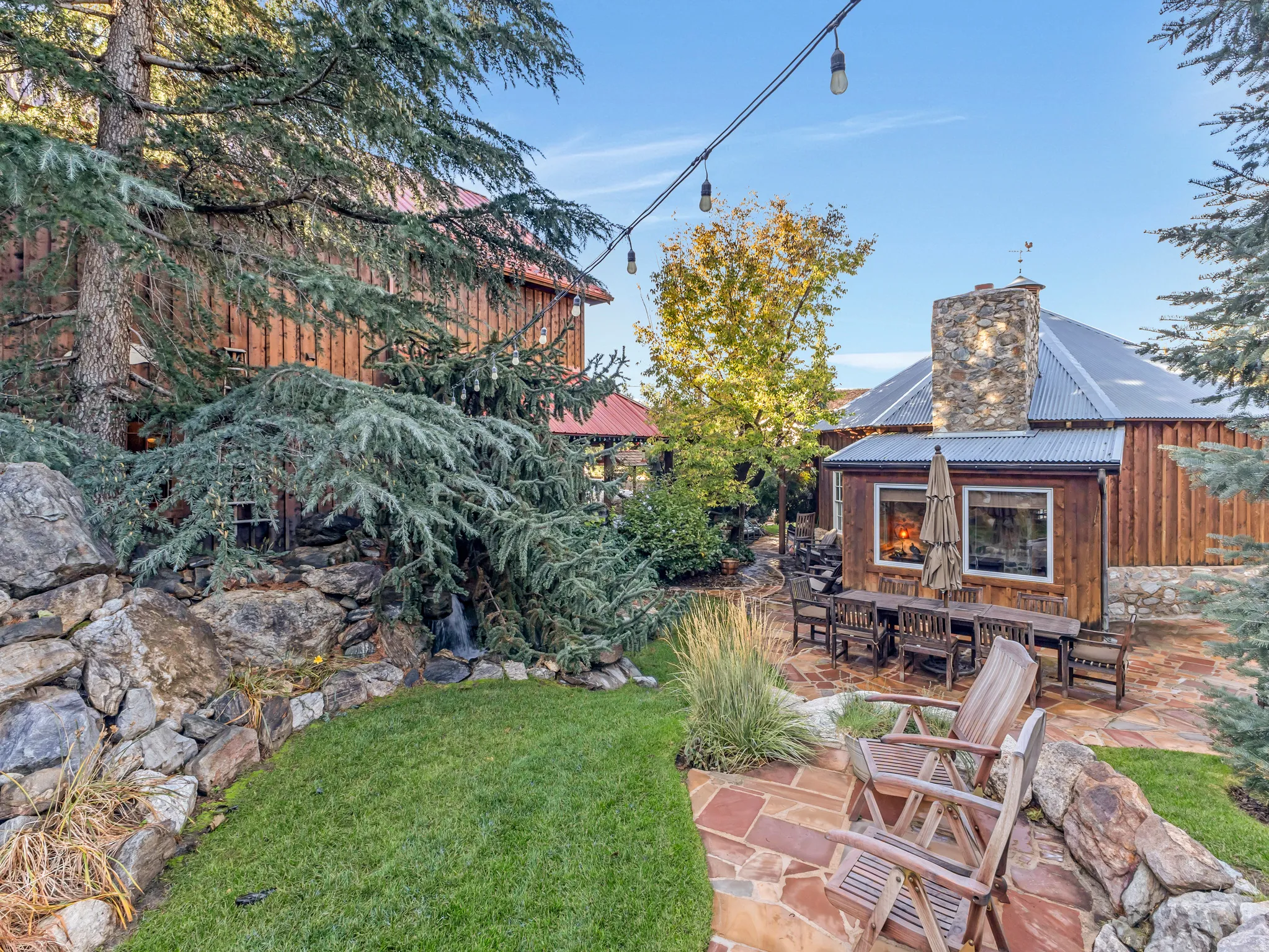 Outdoor living space featuring a flagstone patio, manicured lawn, and a natural rock wall with a water feature