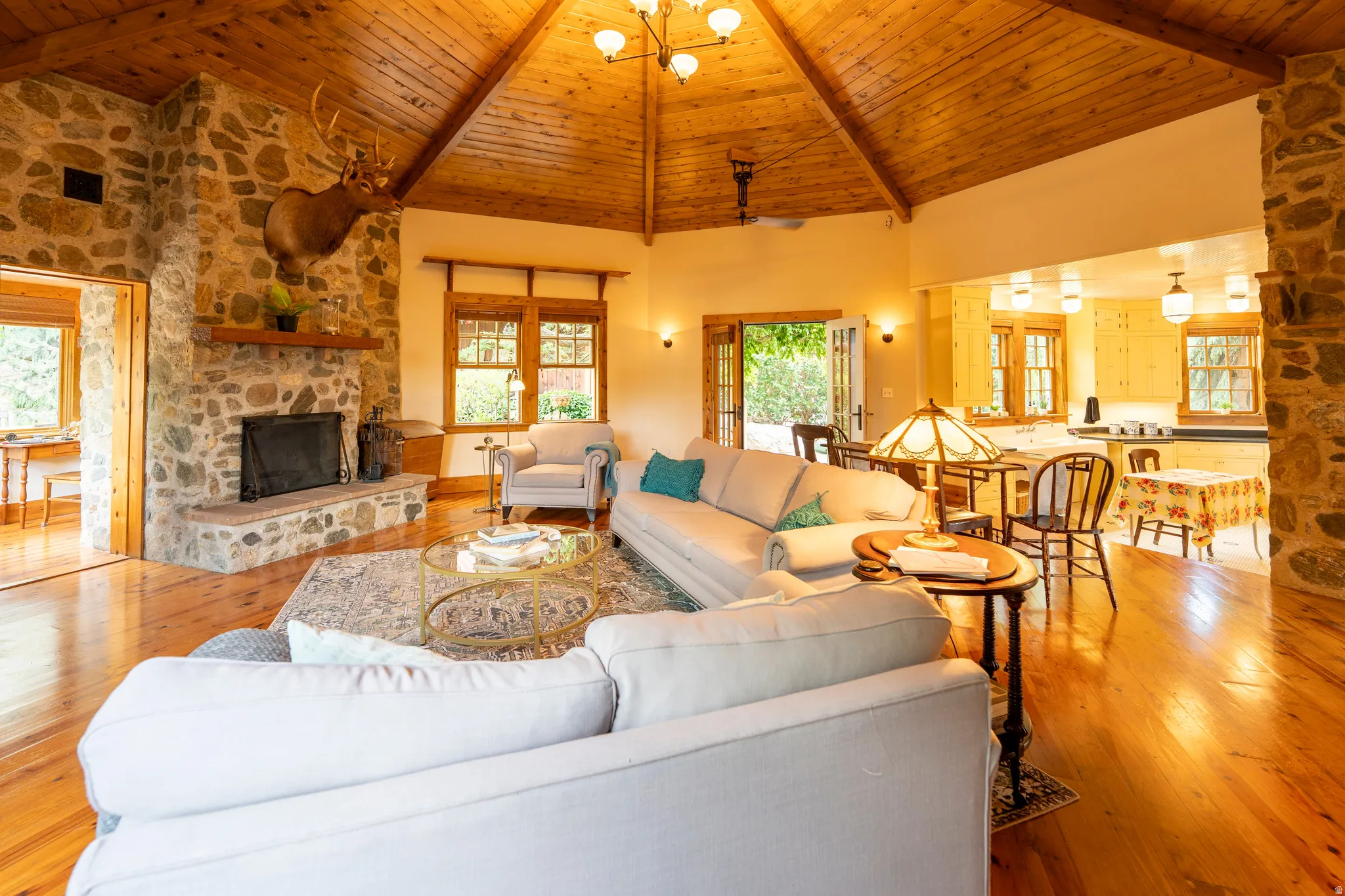 Spacious living area featuring a stone-clad fireplace with a wood mantel, exposed wood-beam vaulted ceiling, and polished wood-finish flooring