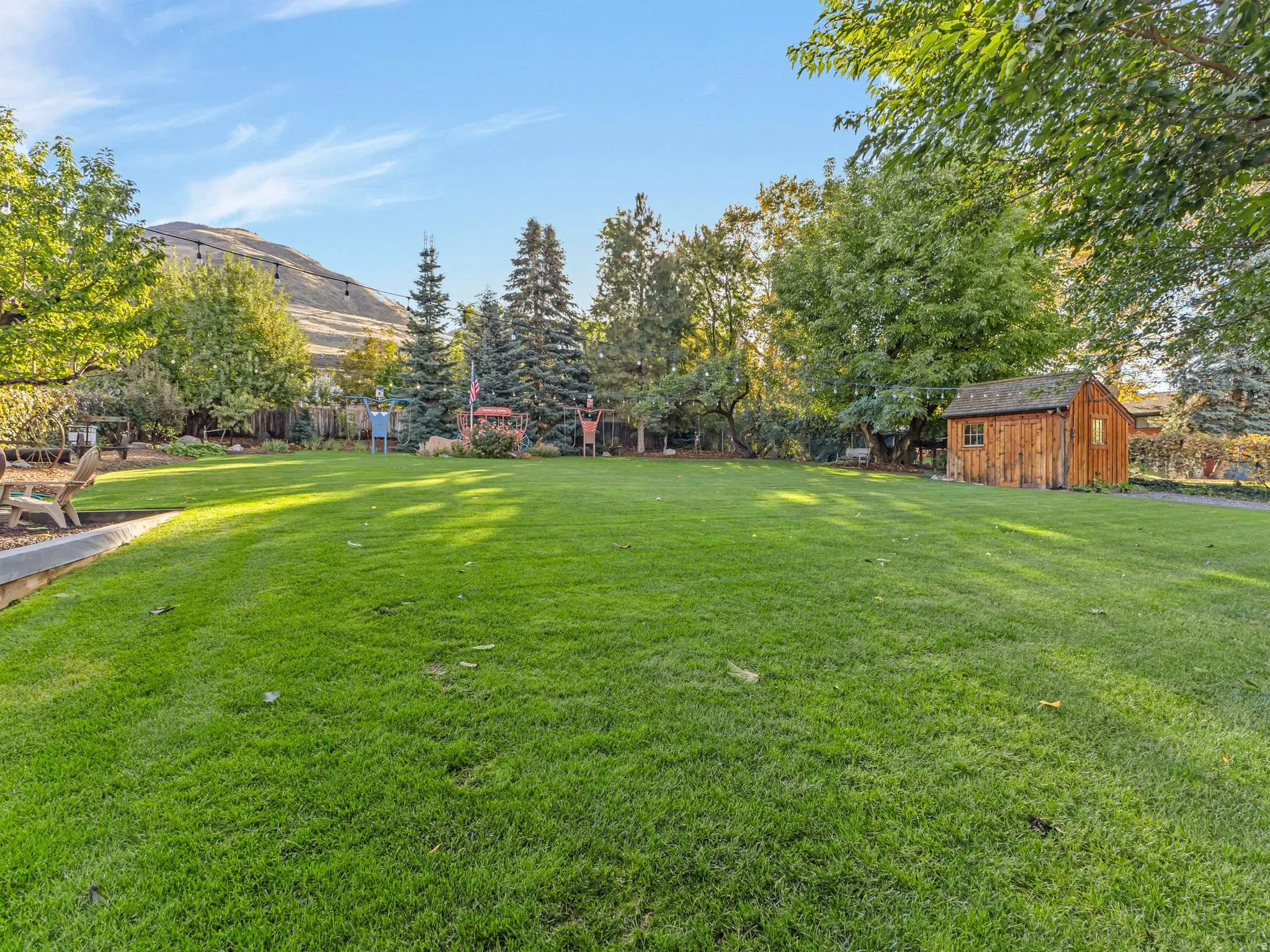 Expansive green lawn with mature trees and a rustic wood-sided shed