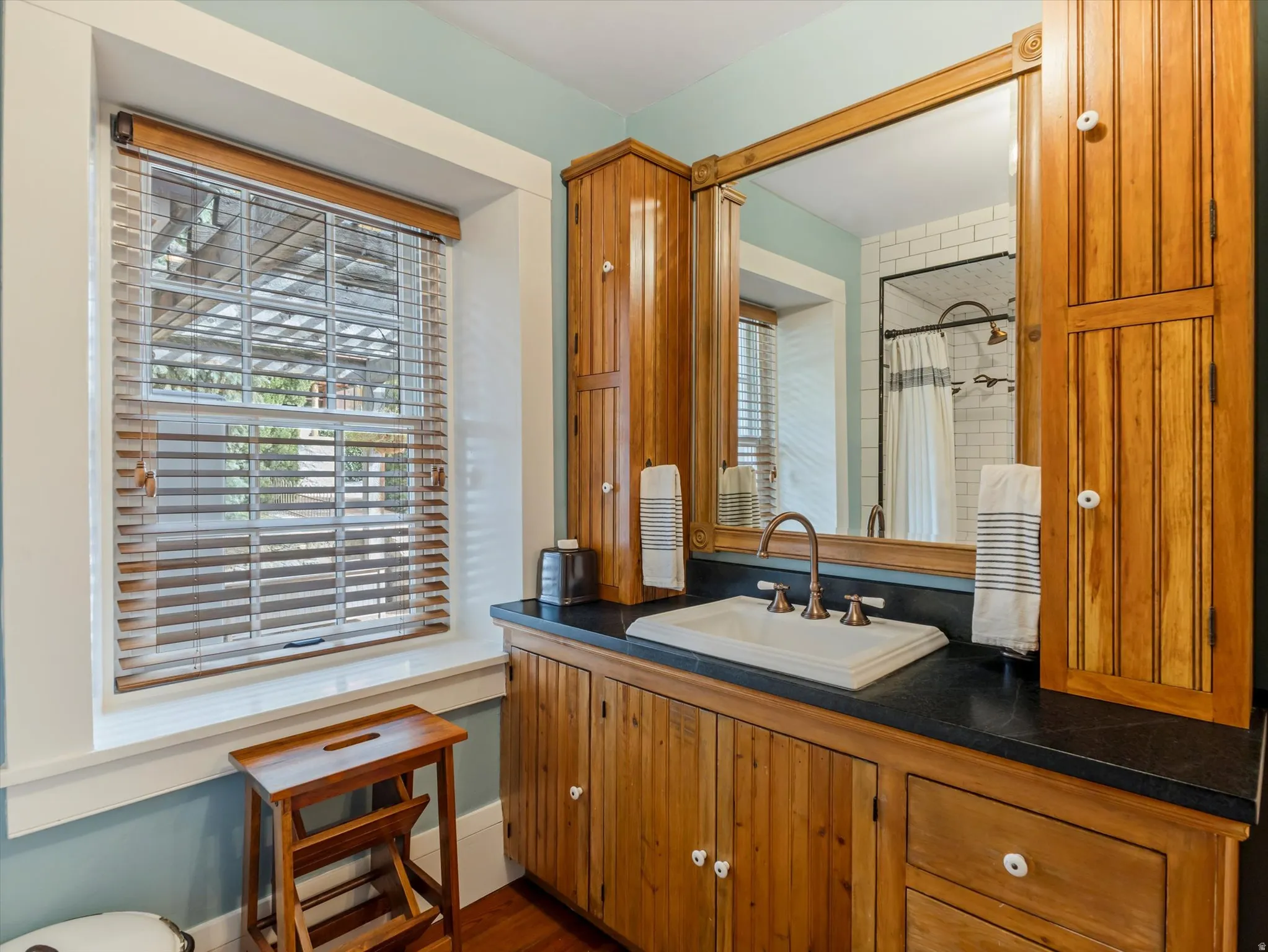 Bathroom featuring a wood-finish vanity with an integrated sink, dark countertop, and a large framed mirror
