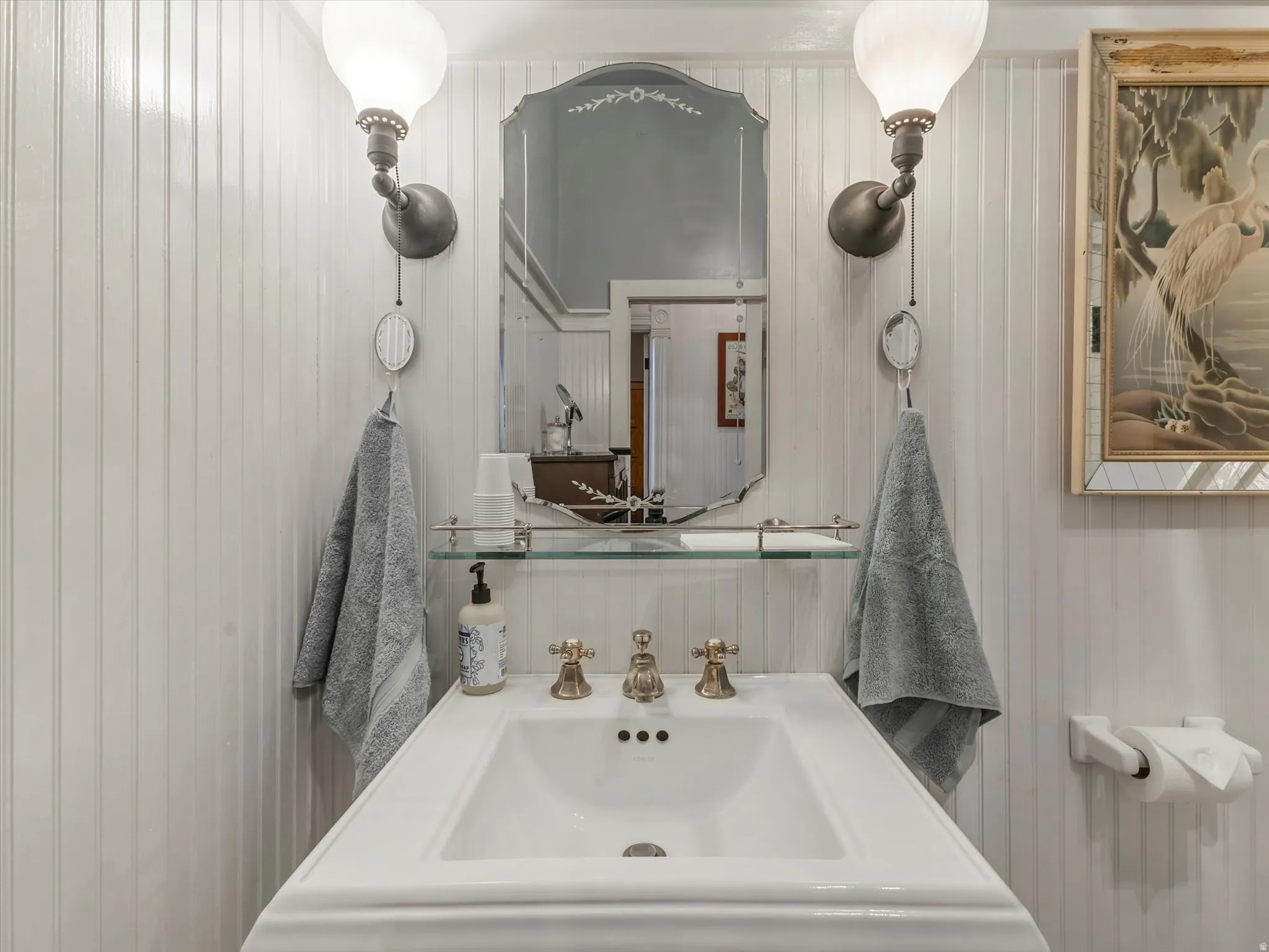 Pedestal sink featuring brass-finish fixtures, a glass shelf, and a framed mirror