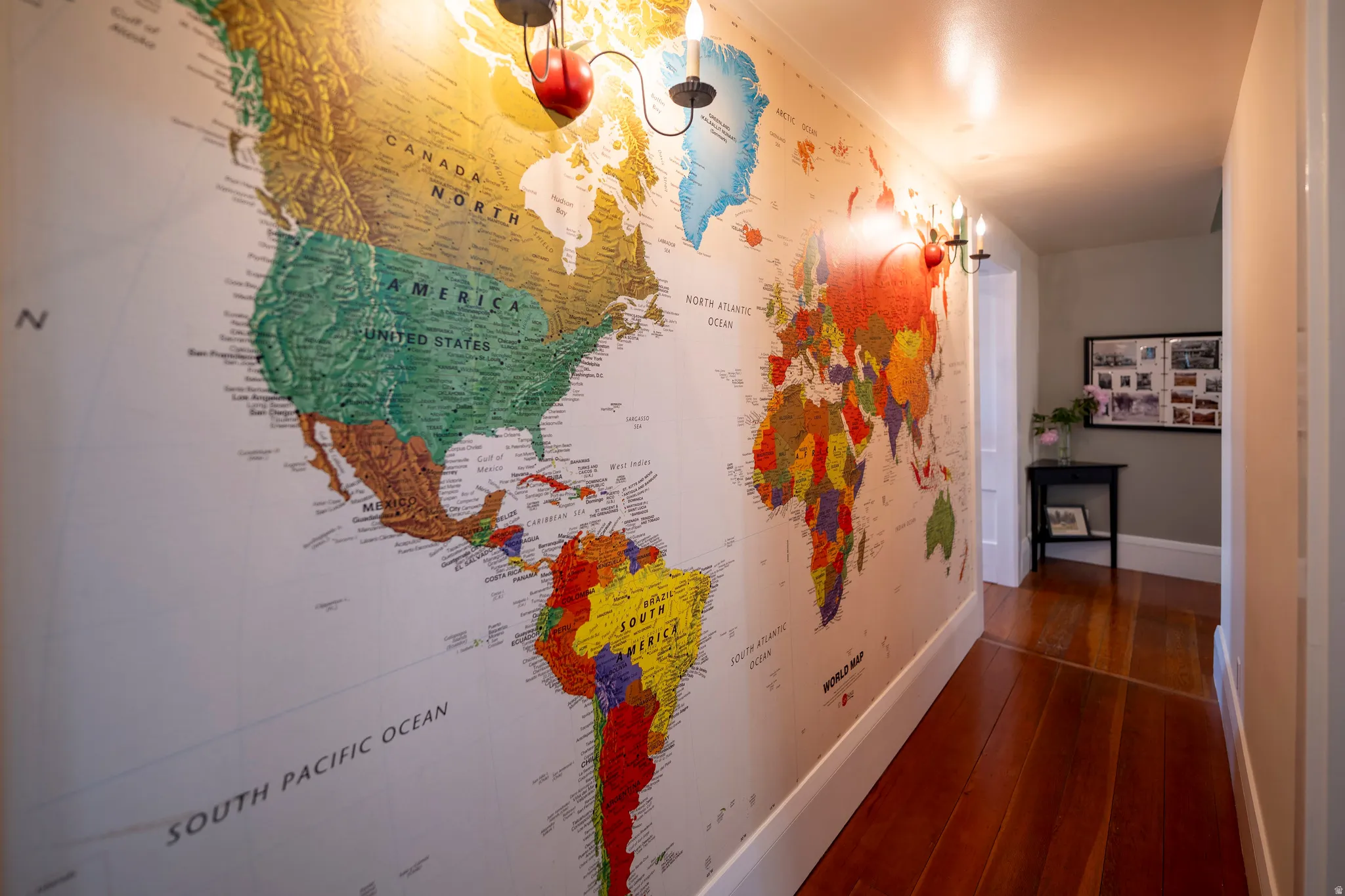 Hallway featuring a large-scale world map wall covering, wood-finish flooring, white baseboards, and wall-mounted light fixtures