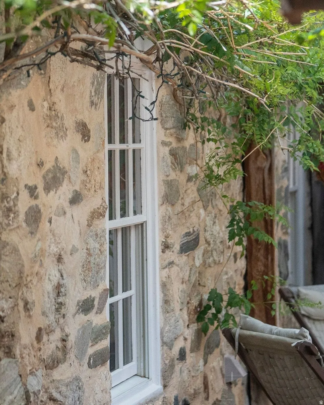 Stone exterior featuring a white-framed window with muntins, natural wood trim, and mature climbing foliage