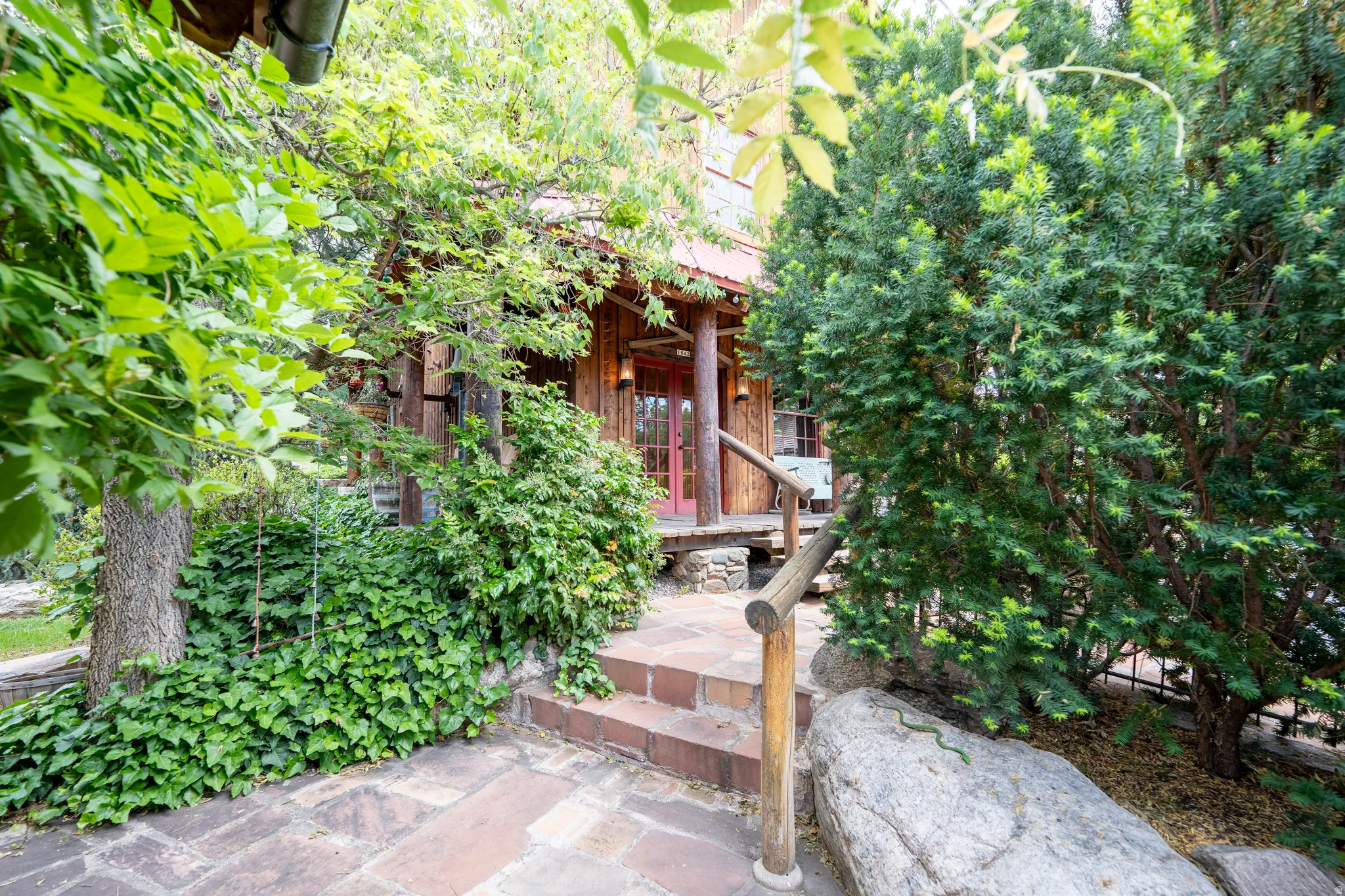Exterior featuring wood siding, a covered porch with round wood columns, and a terraced stone and brick pathway