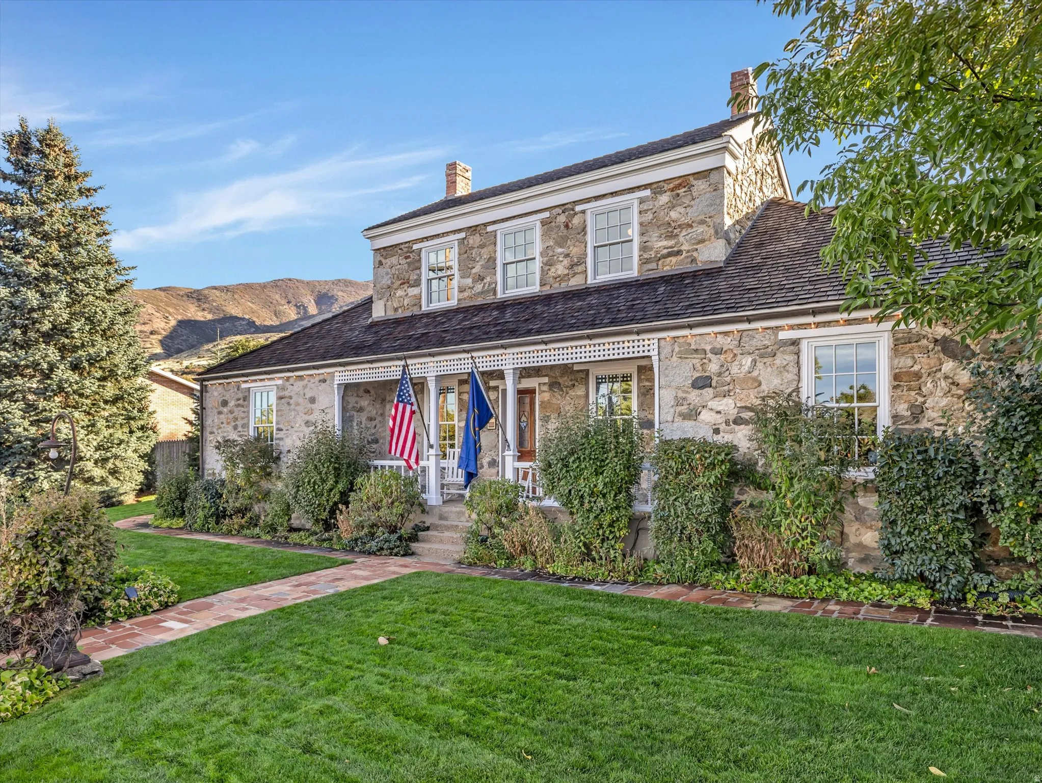 Stone exterior with a full-width front porch, white lattice detailing, and traditional double-hung windows