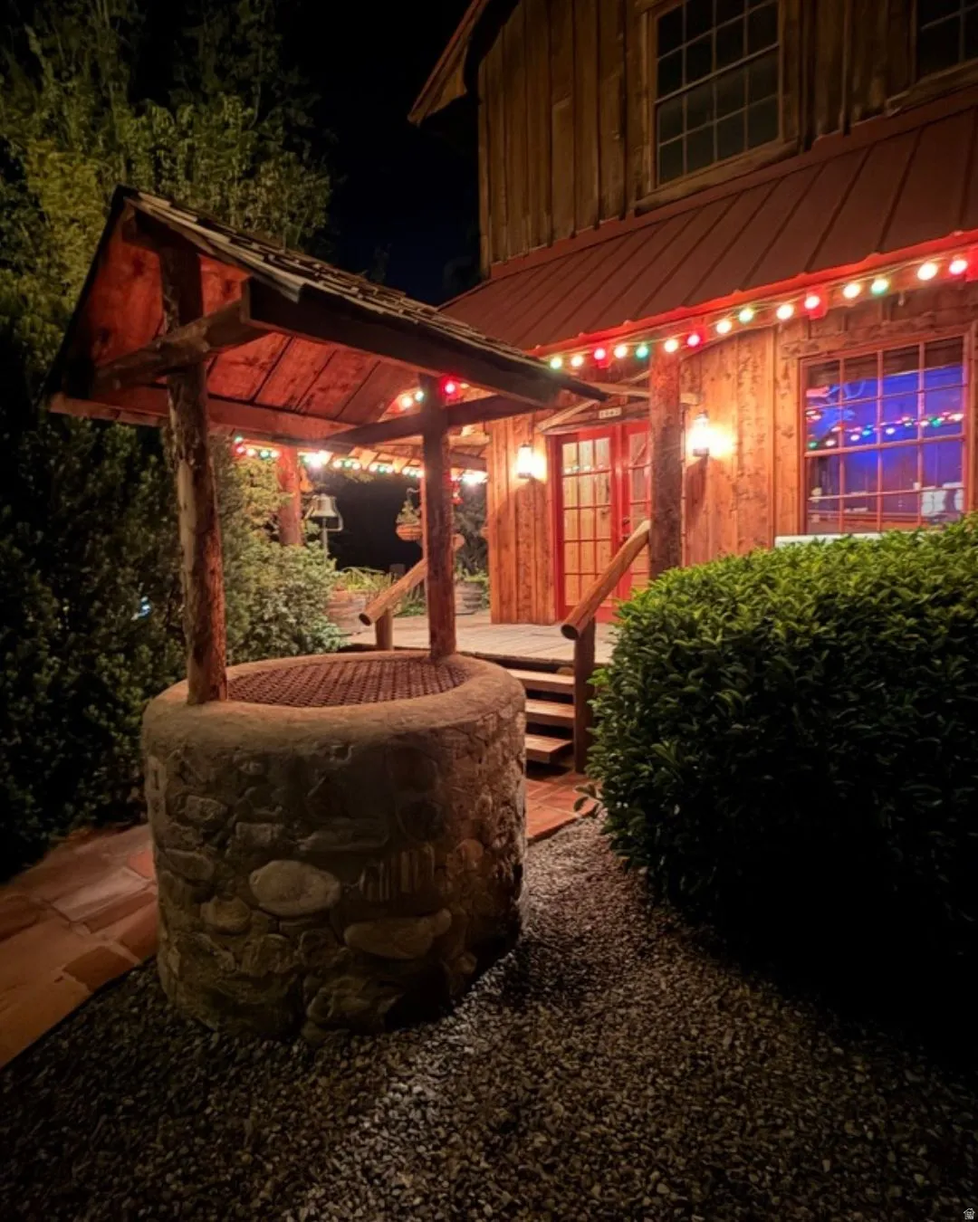 Stone-clad well feature with a wood shingle roof, positioned on a gravel bed