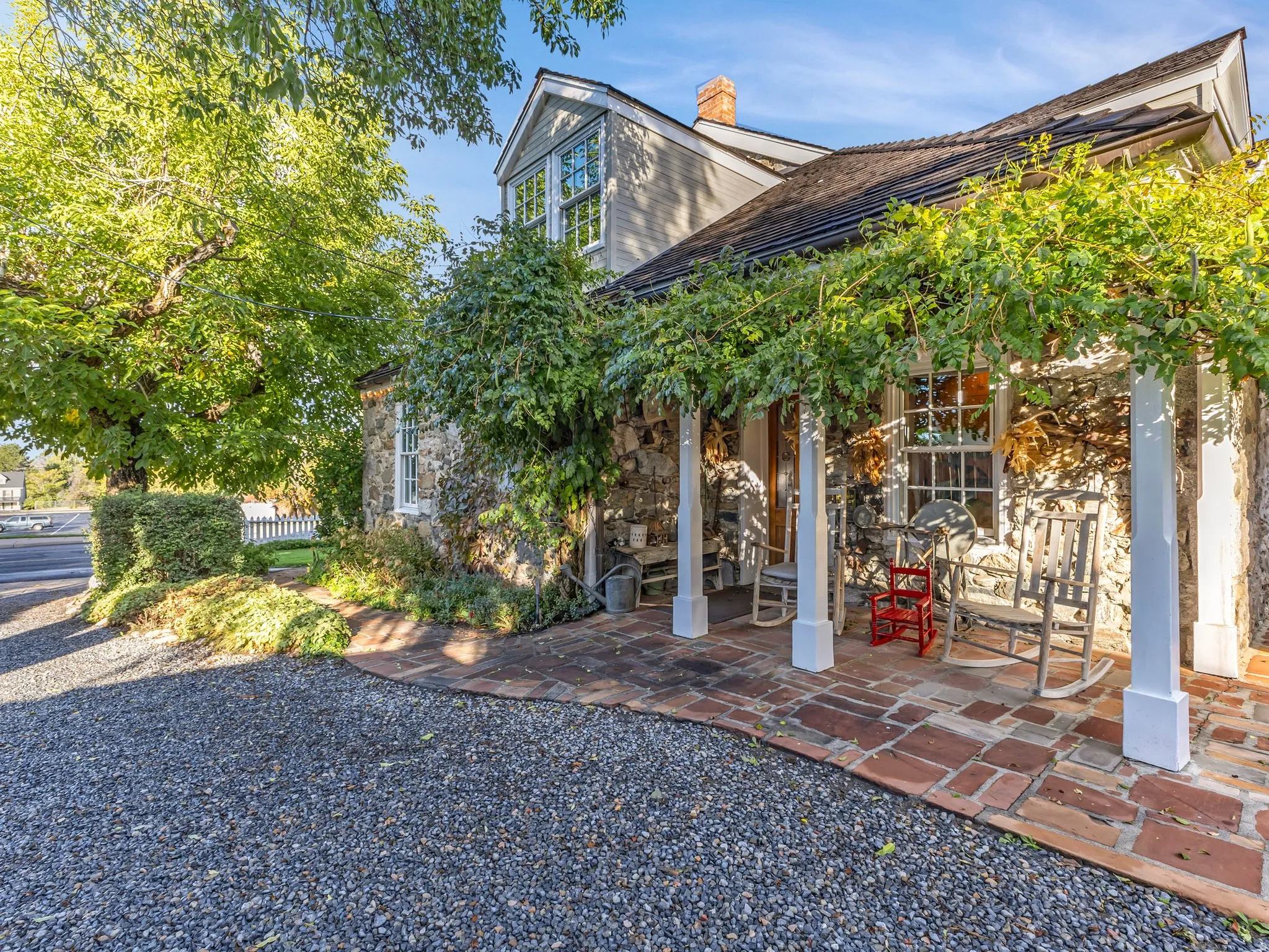 South Side Stone home featuring a covered porch with brick flooring, white support columns, and an overhead vine-covered trellis
