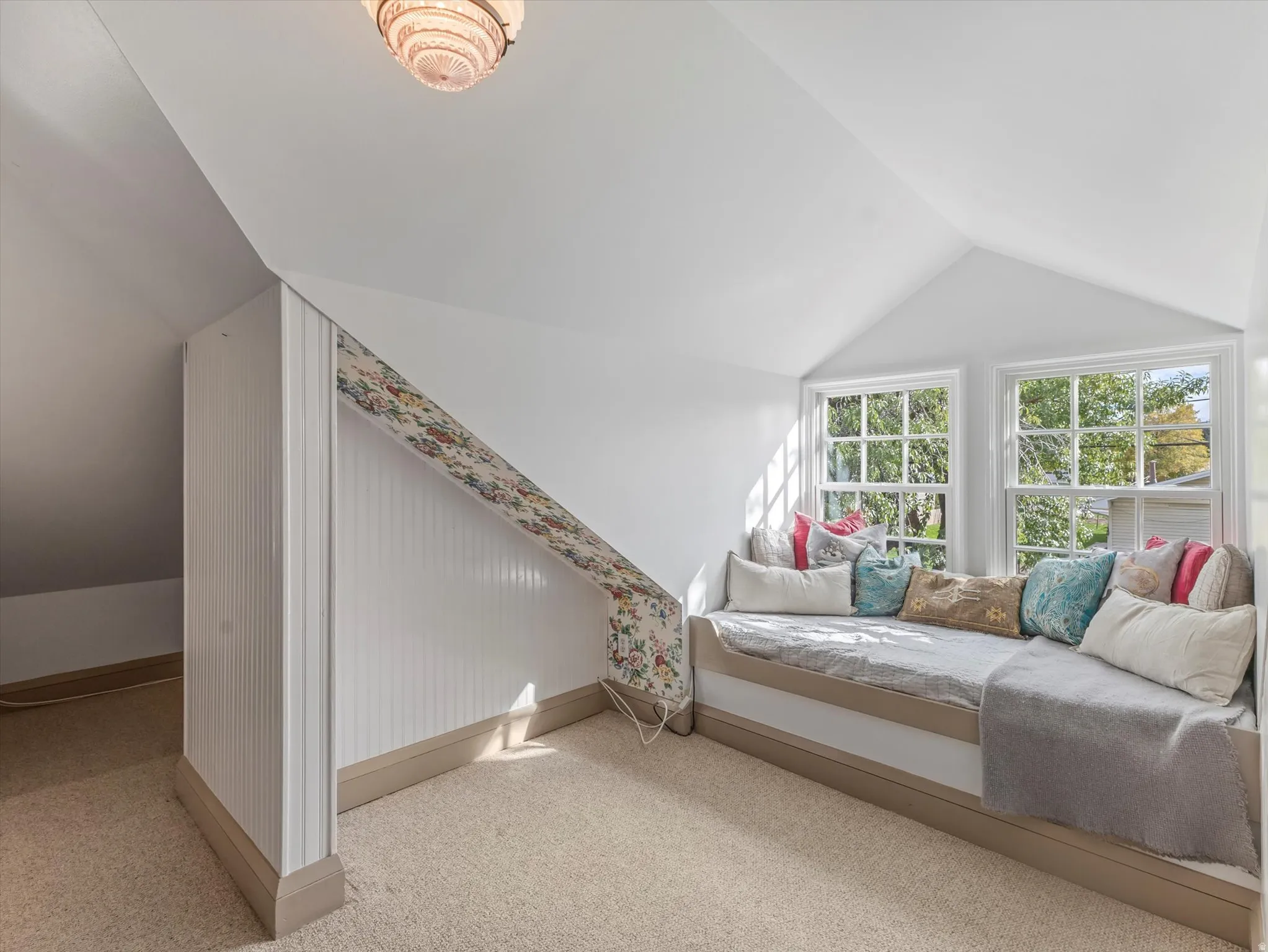 Attic space featuring a built-in window seat, two large windows, vaulted ceilings, and carpeted flooring