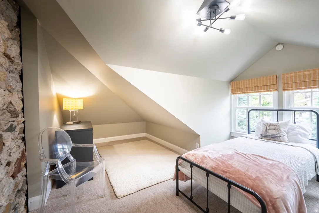 Bedroom featuring sloped ceilings, a prominent stone accent wall, and carpet flooring