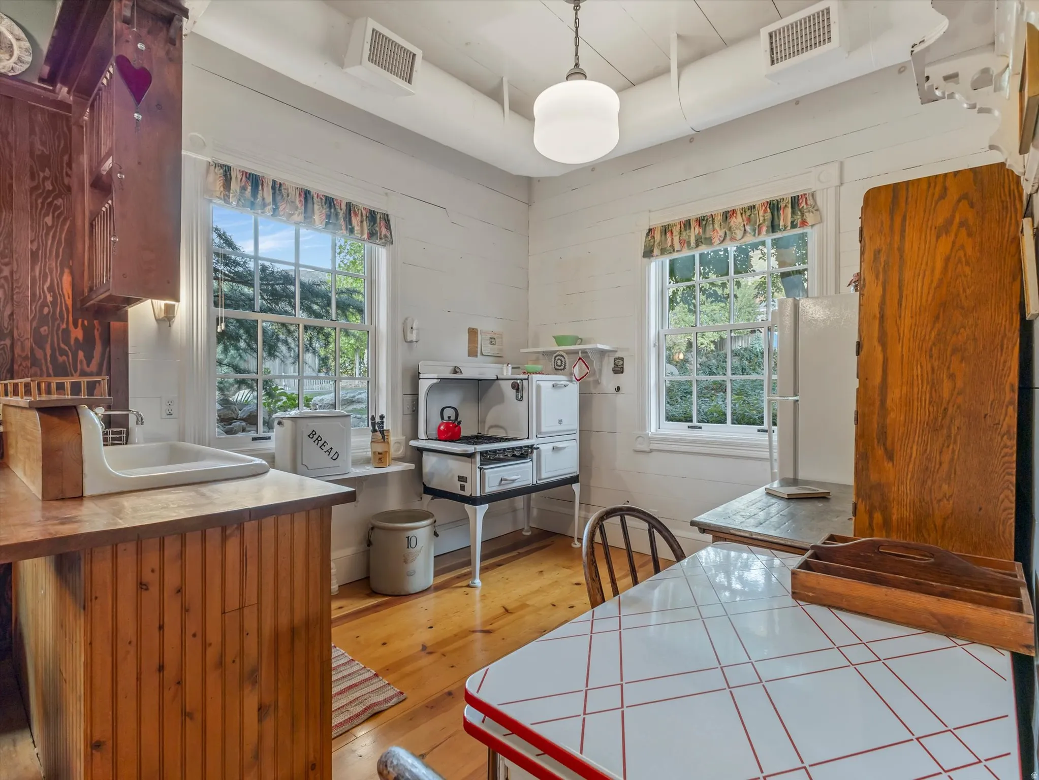 ADU Kitchen featuring wood-finish flooring, two large windows, exposed ceiling ductwork, and a white wall oven with stovetop