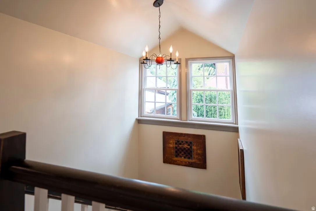 Stairwell with an angled ceiling, featuring a dark metal chandelier, two white-framed windows, and a dark wood handrail