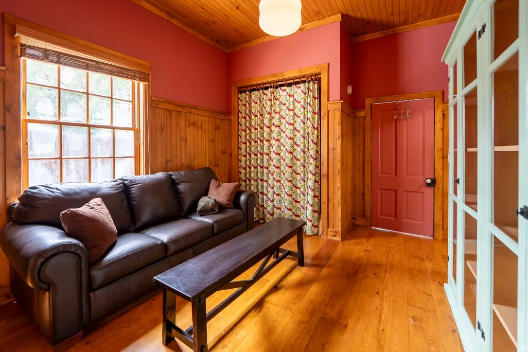 Guest bedroom in ADU. Hardwood flooring throughout featuring wood paneling on lower walls, a wood-finish ceiling, and a multi-pane window with a wood frame