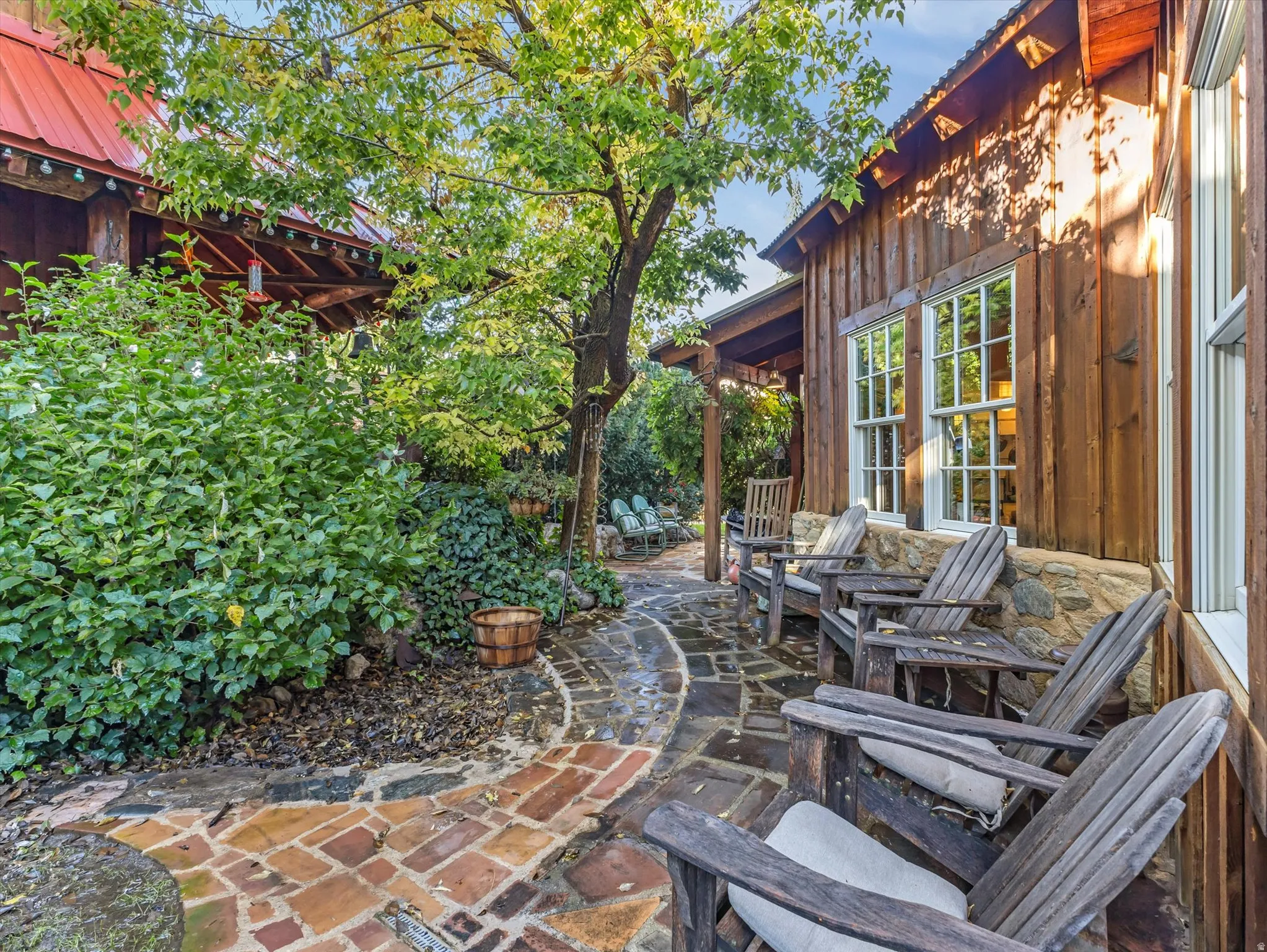 Outdoor patio featuring a flagstone and brick-paver pathway, bordered by lush greenery