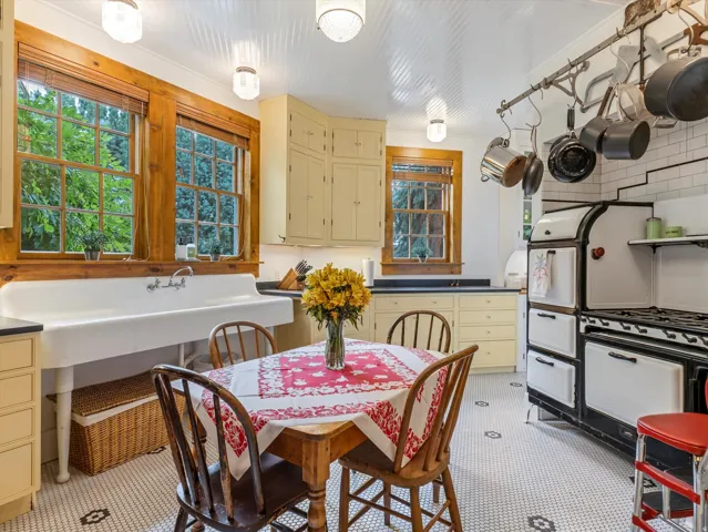 Kitchen featuring a classic white farmhouse sink, mosaic tile flooring, cream-painted cabinetry, a vintage-style range, and natural wood window trim