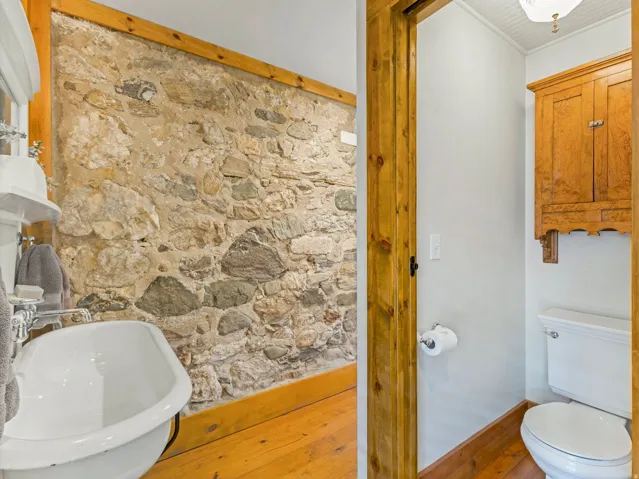 Exposed stone wall detailing a white pedestal sink with polished chrome fixtures and light wood-finish flooring
