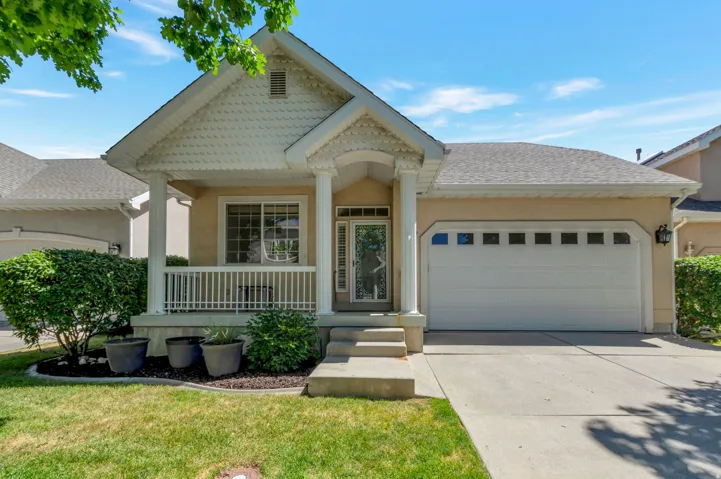 Front exterior featuring a covered porch with white railing, decorative columns, a gabled entry with shingle siding, an attached garage with window inserts, and a concrete driveway