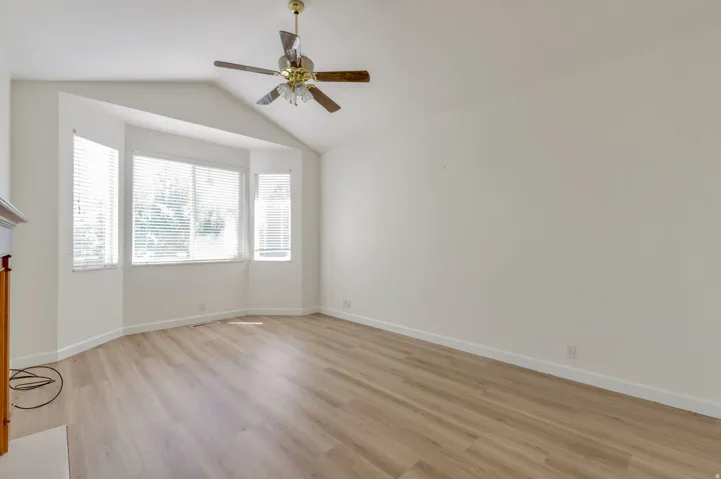 Bright interior space featuring a bay window, vaulted ceiling, wood-finish flooring, and a ceiling fan with integrated lighting