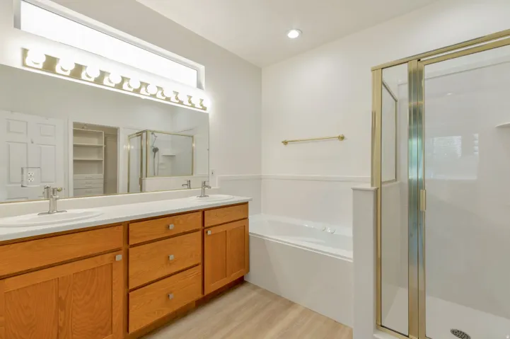 Bathroom featuring a double vanity with wood cabinetry and undermount sinks, a large mirror, a separate shower with a glass enclosure, and a built-in tub