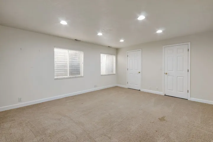 Carpeted room featuring recessed lighting, two windows with blinds, and two paneled doors