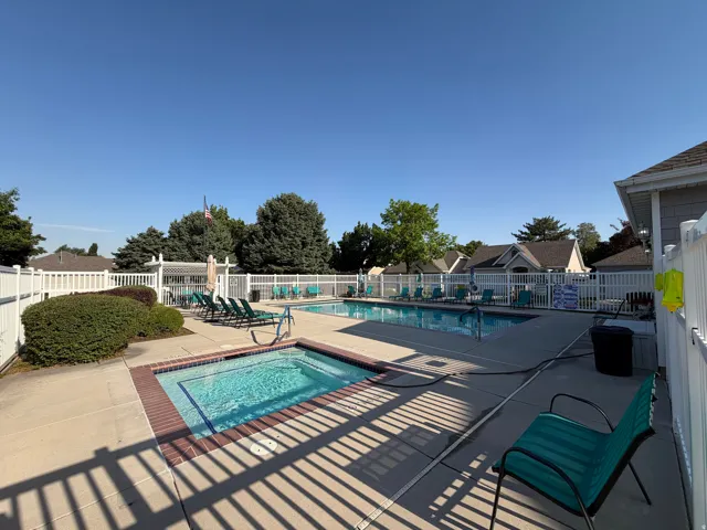 Community swimming pool and spa with surrounding concrete decking, enclosed by a white picket fence