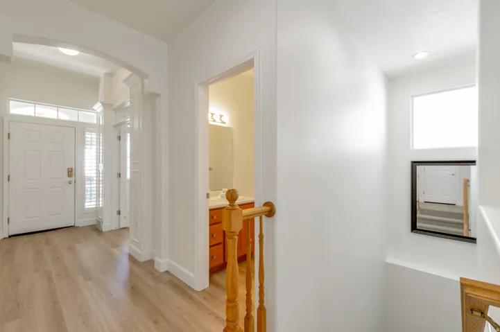 Entryway featuring wood-finish flooring, a white paneled front door with transom window, and an adjacent hall bath with a wood vanity and mirror