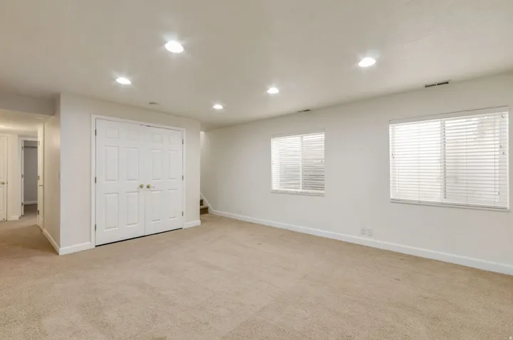 Spacious room featuring neutral carpeting, recessed lighting, and two windows with horizontal blinds