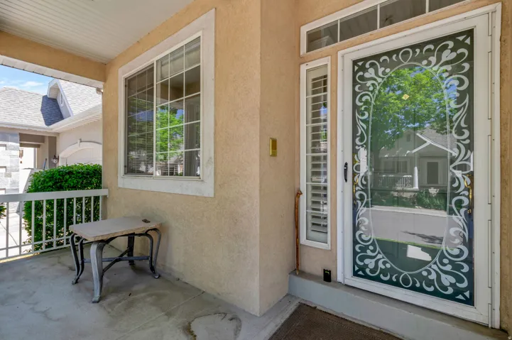 Covered front porch featuring a decorative storm door with sidelight, transom windows, and an adjacent window with grid panes