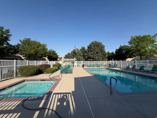 Community pool area featuring a rectangular swimming pool, a separate spa, surrounding concrete deck, and white picket fencing