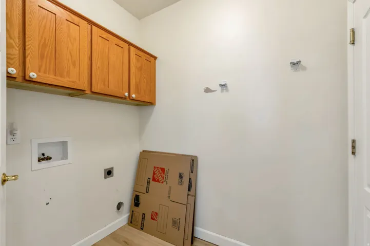 Utility space featuring upper wood cabinetry with white knobs, wood-finish flooring, and white baseboards