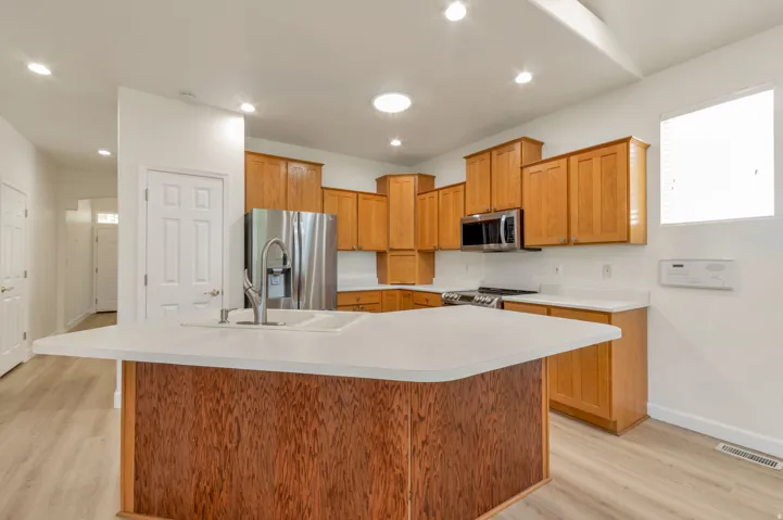 Kitchen featuring an island with a white countertop and integrated sink, stainless steel appliances, light wood-finish cabinetry, and recessed lighting