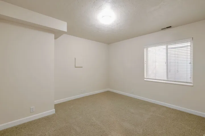 Carpeted interior room with neutral-toned walls, white trim, a ceiling-mounted light fixture, and a window with horizontal blinds