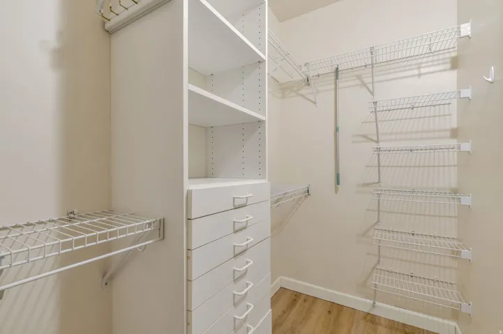 Walk-in closet featuring white built-in shelving, multiple wire rack shelves, a built-in dresser with seven drawers, and light wood-finish flooring