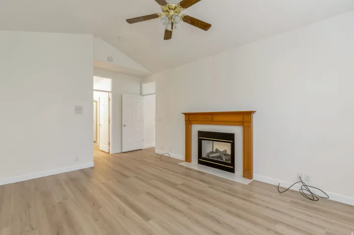 Living space featuring a fireplace with a wood mantle and hearth, wood-finish flooring, vaulted ceiling, and a ceiling fan